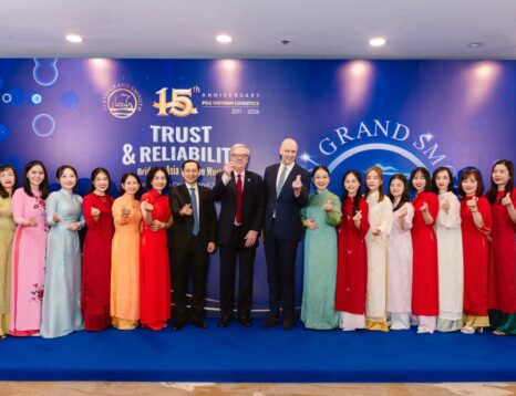 Group of people in colorful Vietnamese ao dai posing for a group photo on a blue carpet, with a banner commemorating a 15th anniversary behind them.