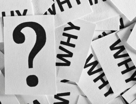 White cards with the word WHY scattered around a central card showing a large question mark, conveying questioning or curiosity.
