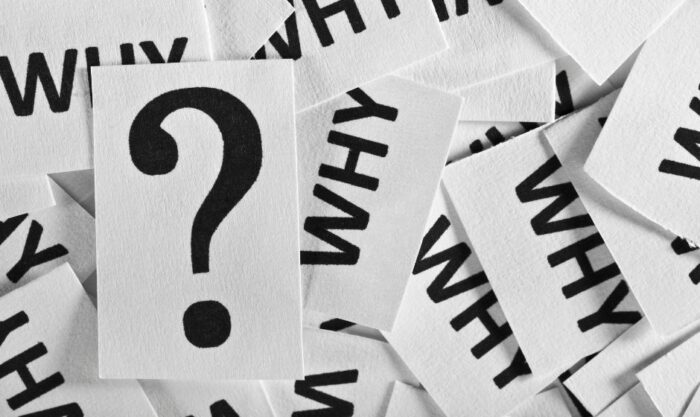 White cards with the word WHY scattered around a central card showing a large question mark, conveying questioning or curiosity.