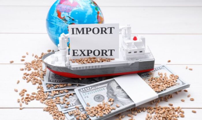 Toy cargo ship with an 'IMPORT EXPORT' sign atop money and scattered grains, symbolizing international trade.