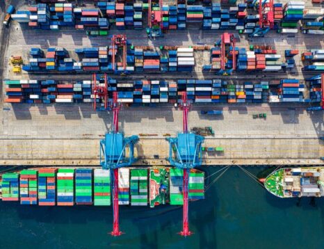 Aerial view of a busy shipping port with stacked colorful containers and large blue gantry cranes over the docked ships left and right
