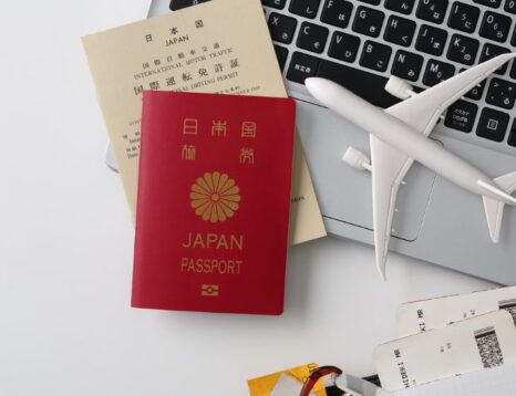 Red Japan passport and beige travel documents placed on a laptop with a small white airplane model nearby, suggesting travel planning.