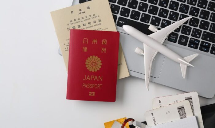 Red Japan passport and beige travel documents placed on a laptop with a small white airplane model nearby, suggesting travel planning.