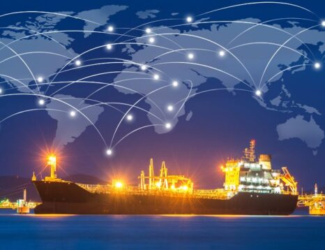 Cargo ship at a illuminated port at night with a glowing global network of white lines across a world map overhead, symbolizing global shipping connectivity