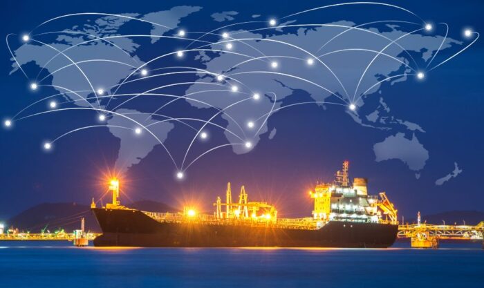 Cargo ship at a illuminated port at night with a glowing global network of white lines across a world map overhead, symbolizing global shipping connectivity